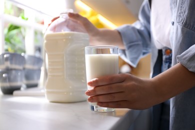 Young woman with gallon bottle of milk and glass at white countertop in kitchen, closeup