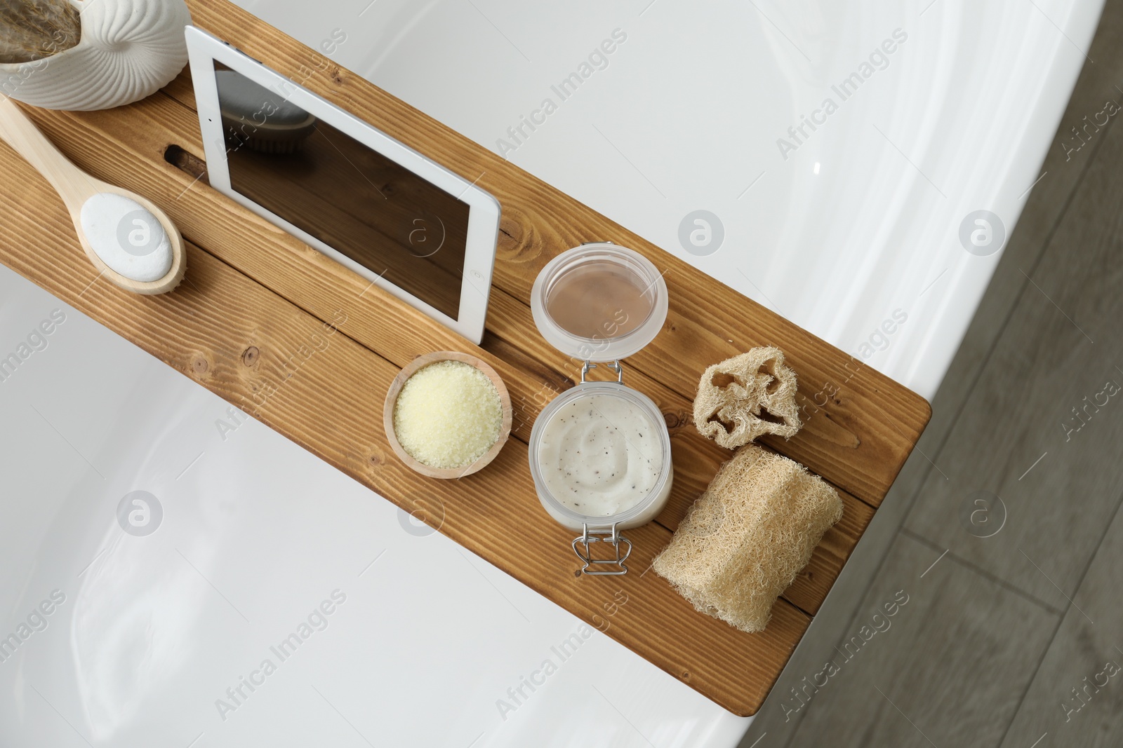 Photo of Wooden tray with tablet and spa products on bath tub in bathroom, top view