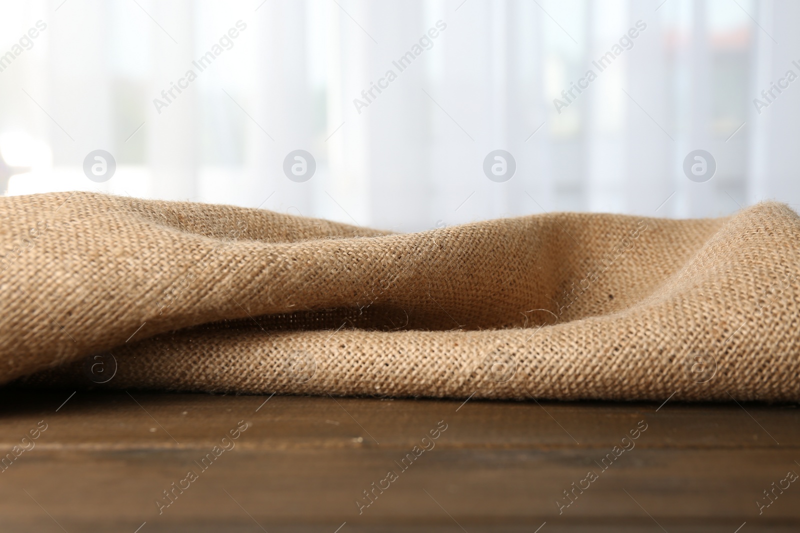 Photo of Brown burlap fabric on wooden table, closeup