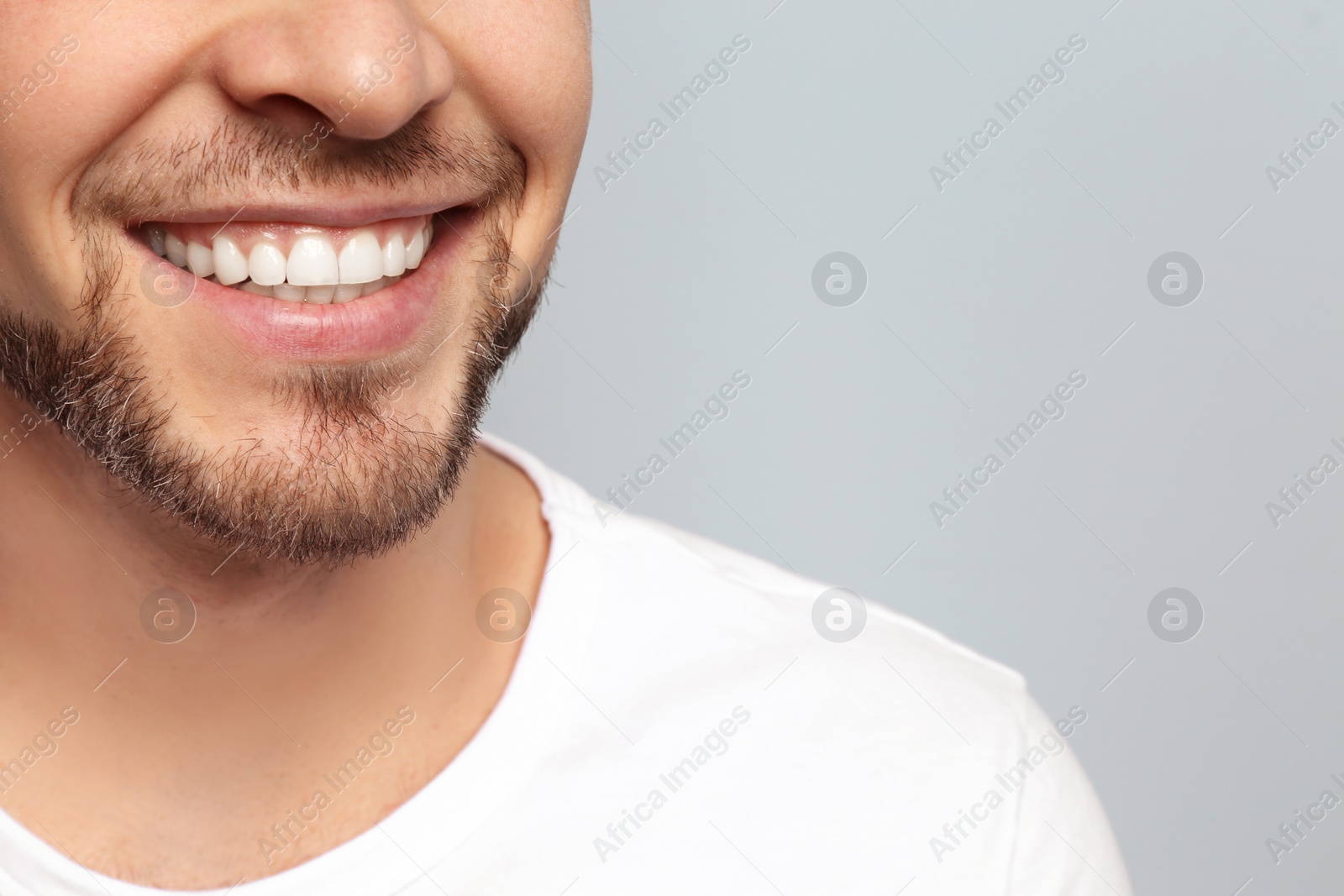 Photo of Young man with beautiful smile on grey background. Teeth whitening