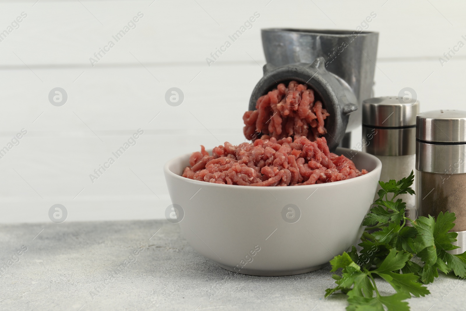 Photo of Mincing beef with manual meat grinder. Parsley and spices on grey table, space for text