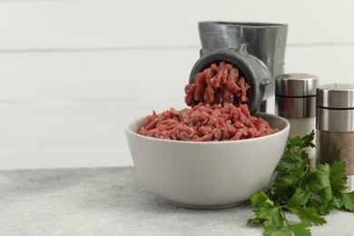 Photo of Mincing beef with manual meat grinder. Parsley and spices on grey table, space for text