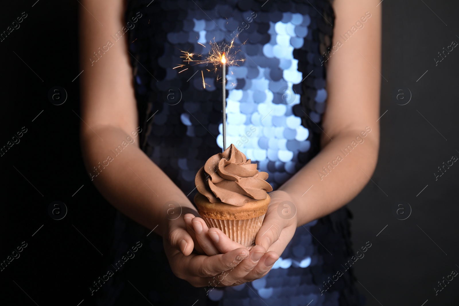 Photo of Woman holding birthday cupcake with sparkler on black background, closeup