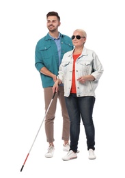 Young man helping blind person with long cane on white background