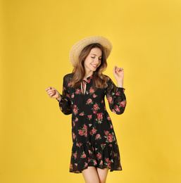 Young woman wearing floral print dress and straw hat on yellow background