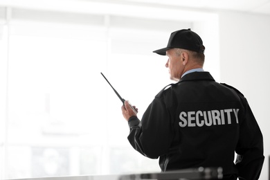 Male security guard using portable radio transmitter on light background