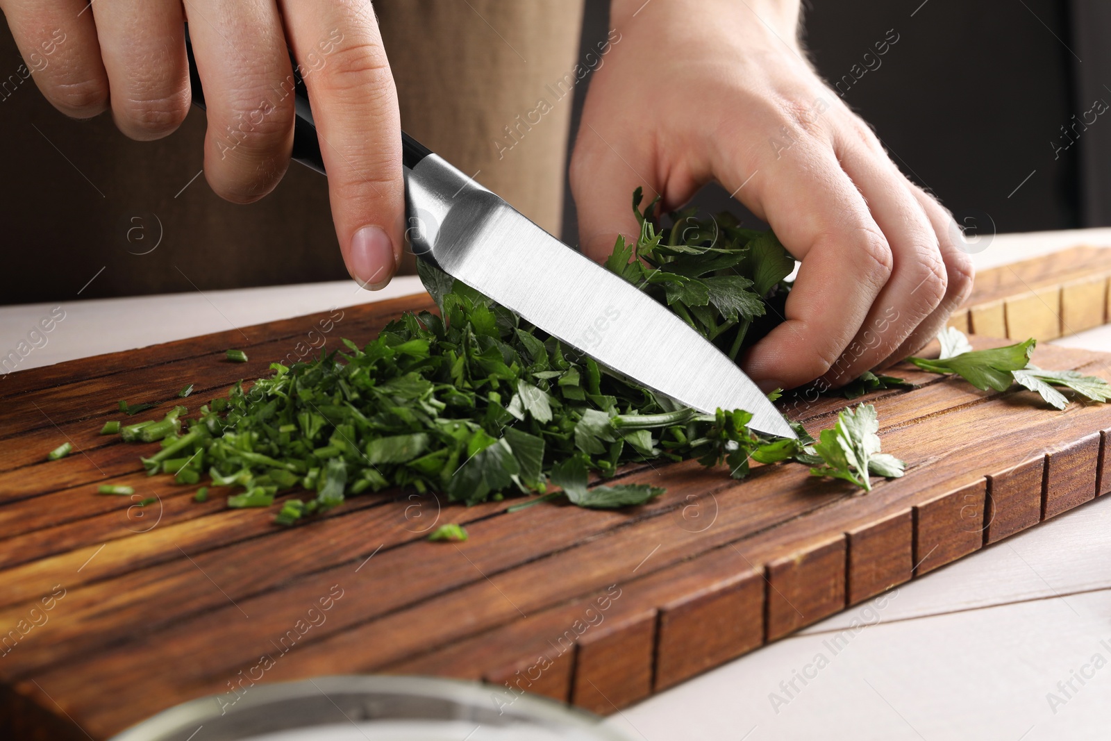 Photo of Woman cutting fresh parsley at white wooden table, closeup