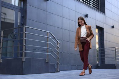 Young woman in formal clothes walking near building outdoors, space for text