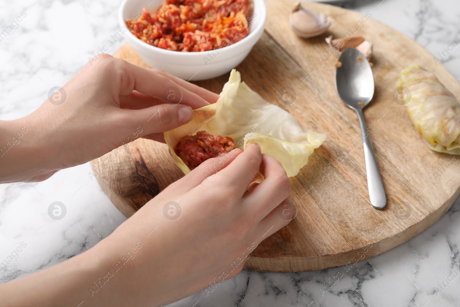 Photo of Woman preparing stuffed cabbage roll at white marble table, closeup