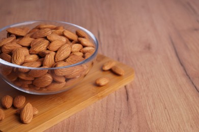 Photo of Bowl of delicious almonds on wooden table. Space for text