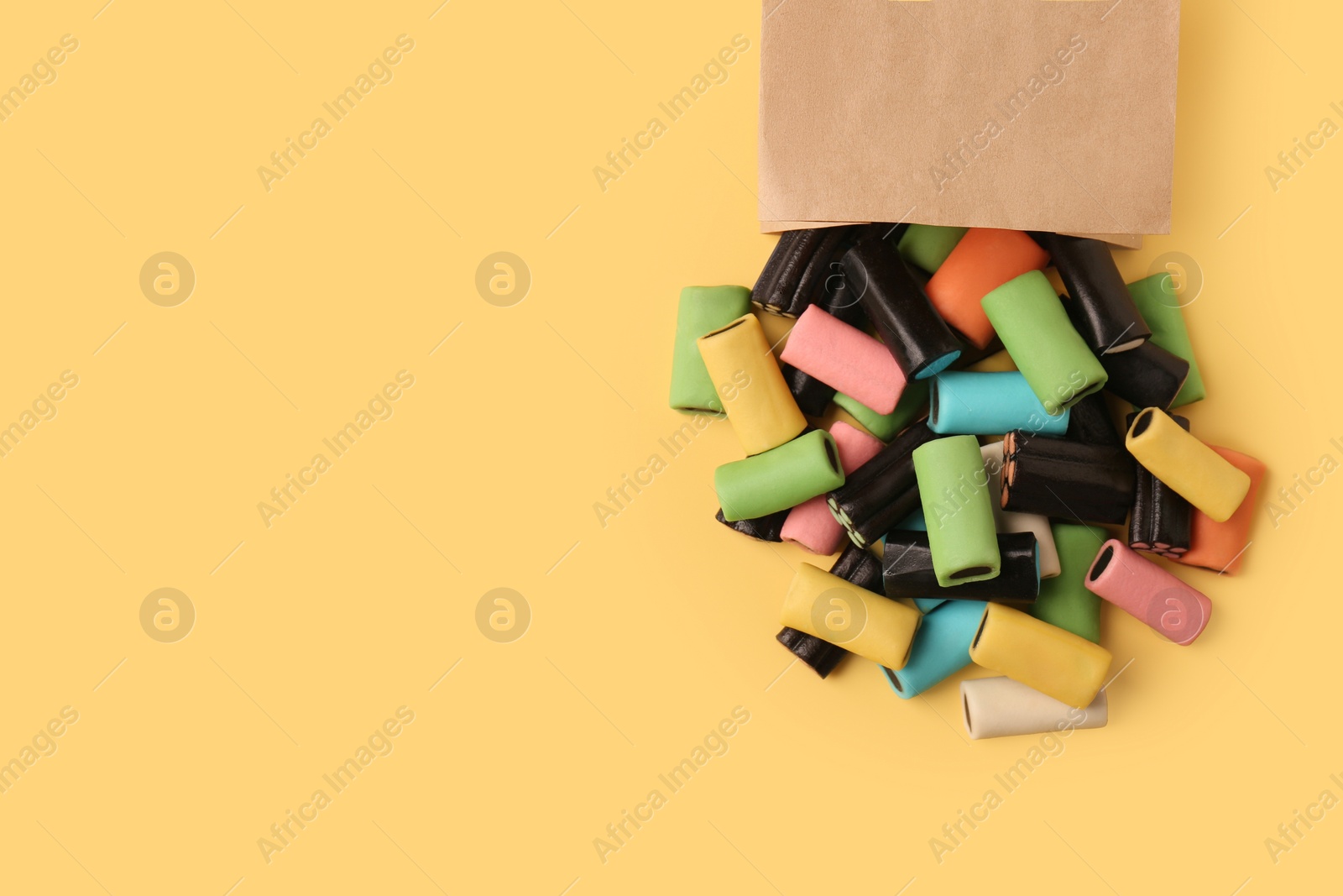 Photo of Tasty liquorice candies and paper bag on yellow background, top view. Space for text