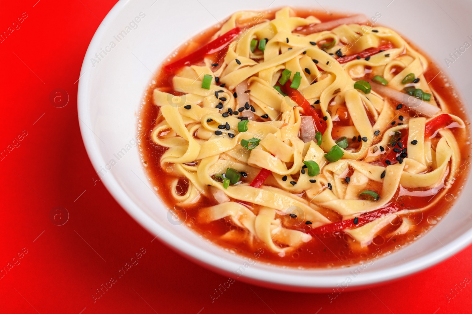 Photo of Plate of asian noodles with broth and vegetables on color background, closeup