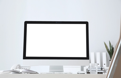 Image of Modern computer with blank screen on table near white wall. Space for design