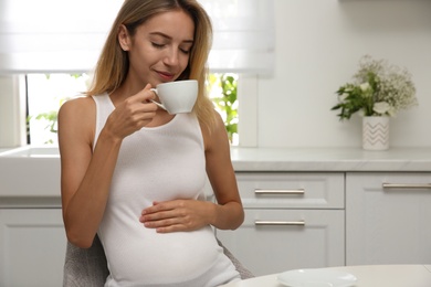 Beautiful pregnant woman drinking tea in kitchen