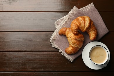 Photo of Delicious fresh croissants and cup of coffee on wooden table, flat lay. Space for text