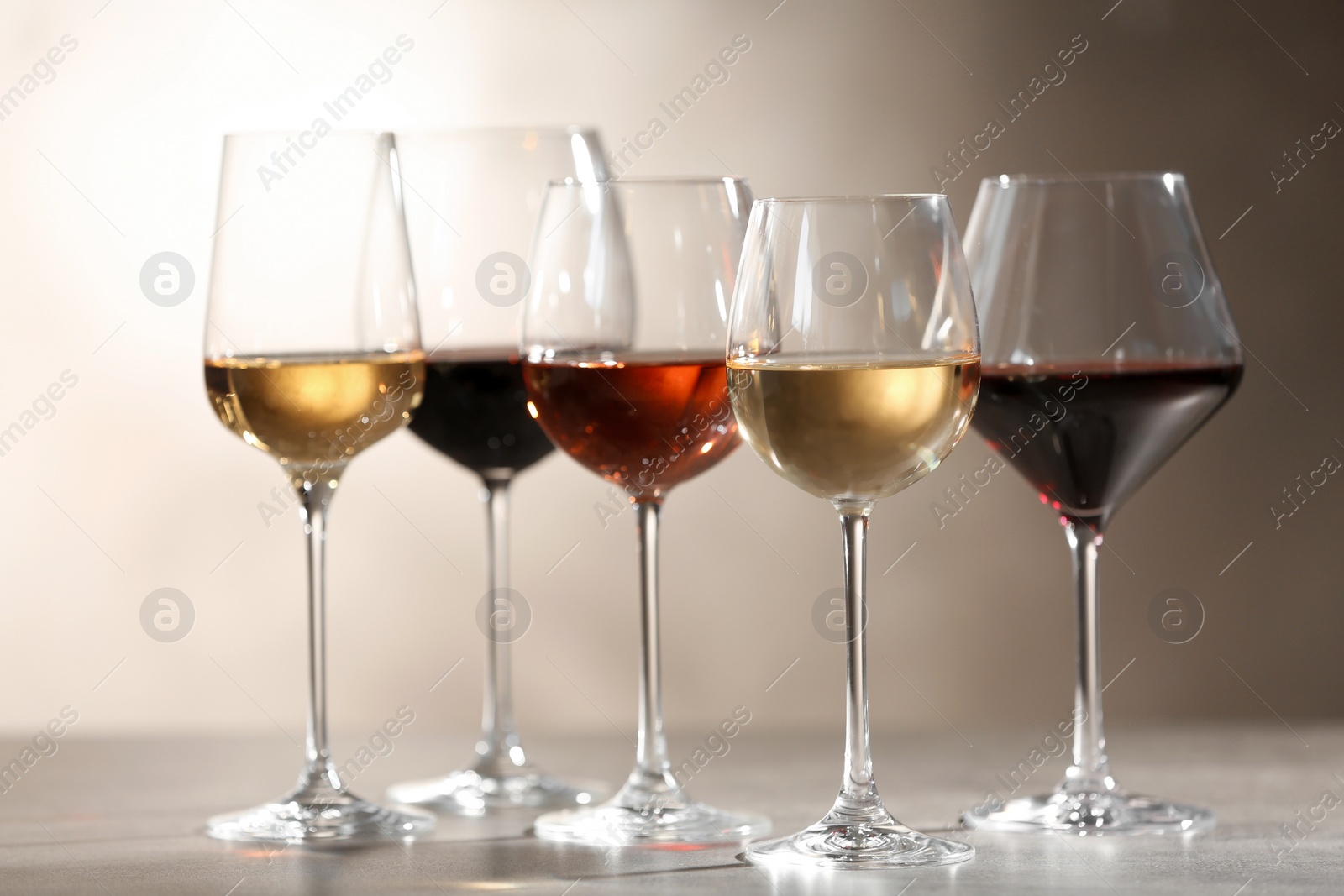 Photo of Glasses with different wines on grey table against light background