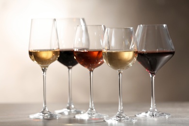 Photo of Glasses with different wines on grey table against light background