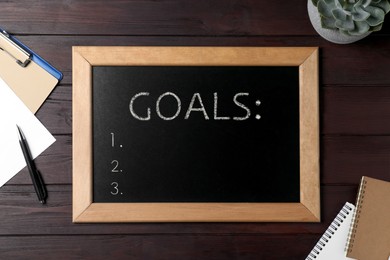Blackboard with word GOALS and empty checklist on wooden background, flat lay