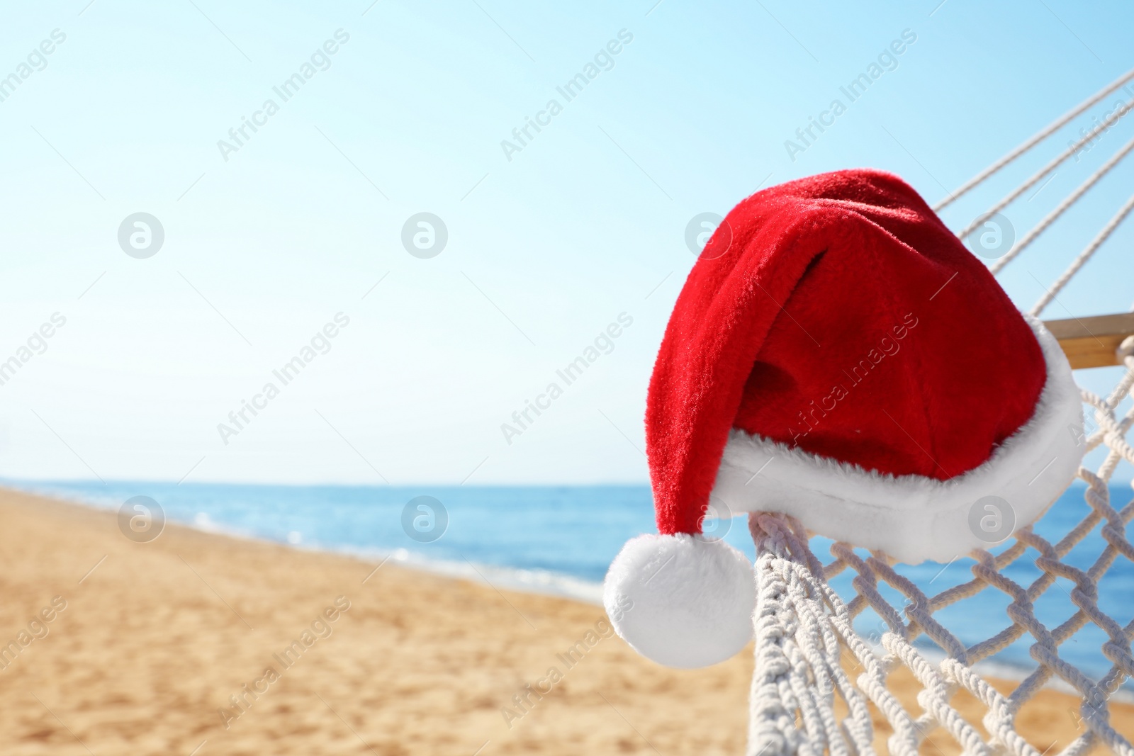 Photo of Rope hammock with Santa's hat on beach, closeup. Christmas vacation