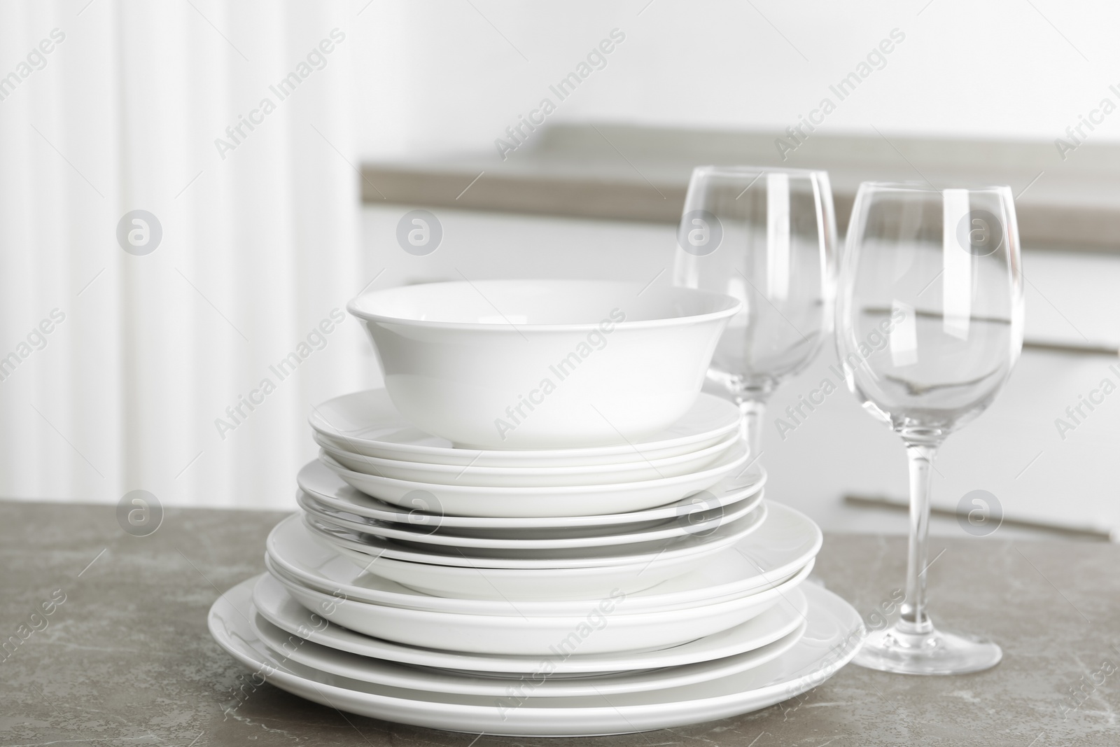Photo of Stack of clean plates and glasses on marble table in kitchen