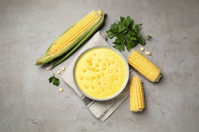 Delicious creamy corn soup and cobs on grey table, flat lay