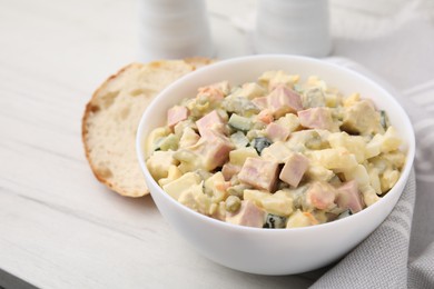 Photo of Tasty Olivier salad with boiled sausage in bowl on white table, closeup. Space for text