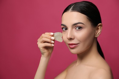 Photo of Beautiful young woman doing facial massage with gua sha tool on pink background