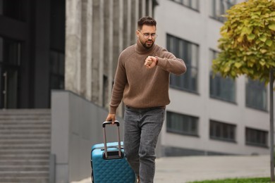 Photo of Being late. Worried man with suitcase looking at watch outdoors