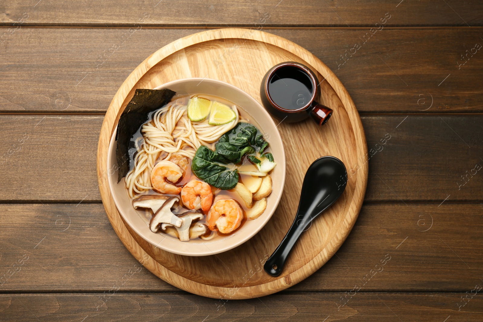 Photo of Delicious ramen with shrimps and mushrooms in bowl served on wooden table, top view. Noodle soup