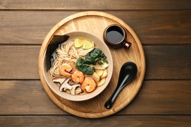 Photo of Delicious ramen with shrimps and mushrooms in bowl served on wooden table, top view. Noodle soup