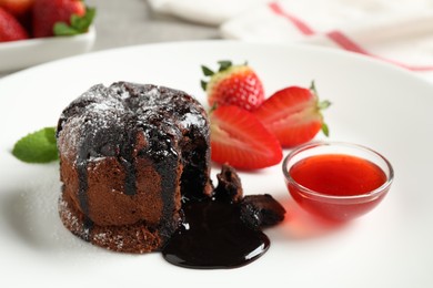 Photo of Delicious warm chocolate lava cake with mint and strawberries on plate, closeup
