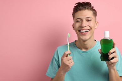 Photo of Young man with mouthwash and toothbrush on pink background, space for text