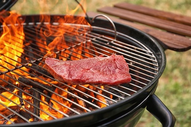 Photo of Tasty meat on barbecue grill with fire flames outdoors, closeup