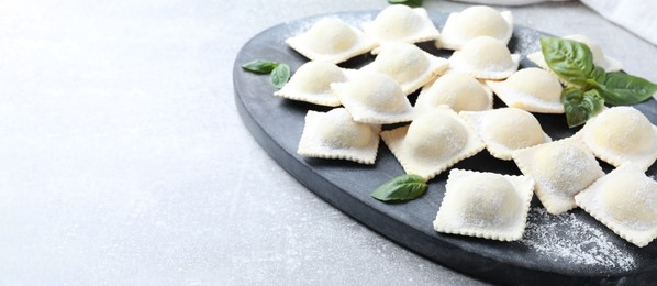 Photo of Homemade uncooked ravioli and basil on grey table