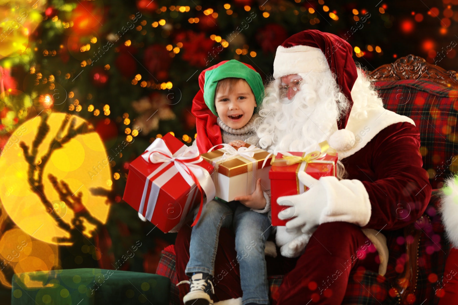 Photo of Santa Claus and little boy with gifts near Christmas tree indoors