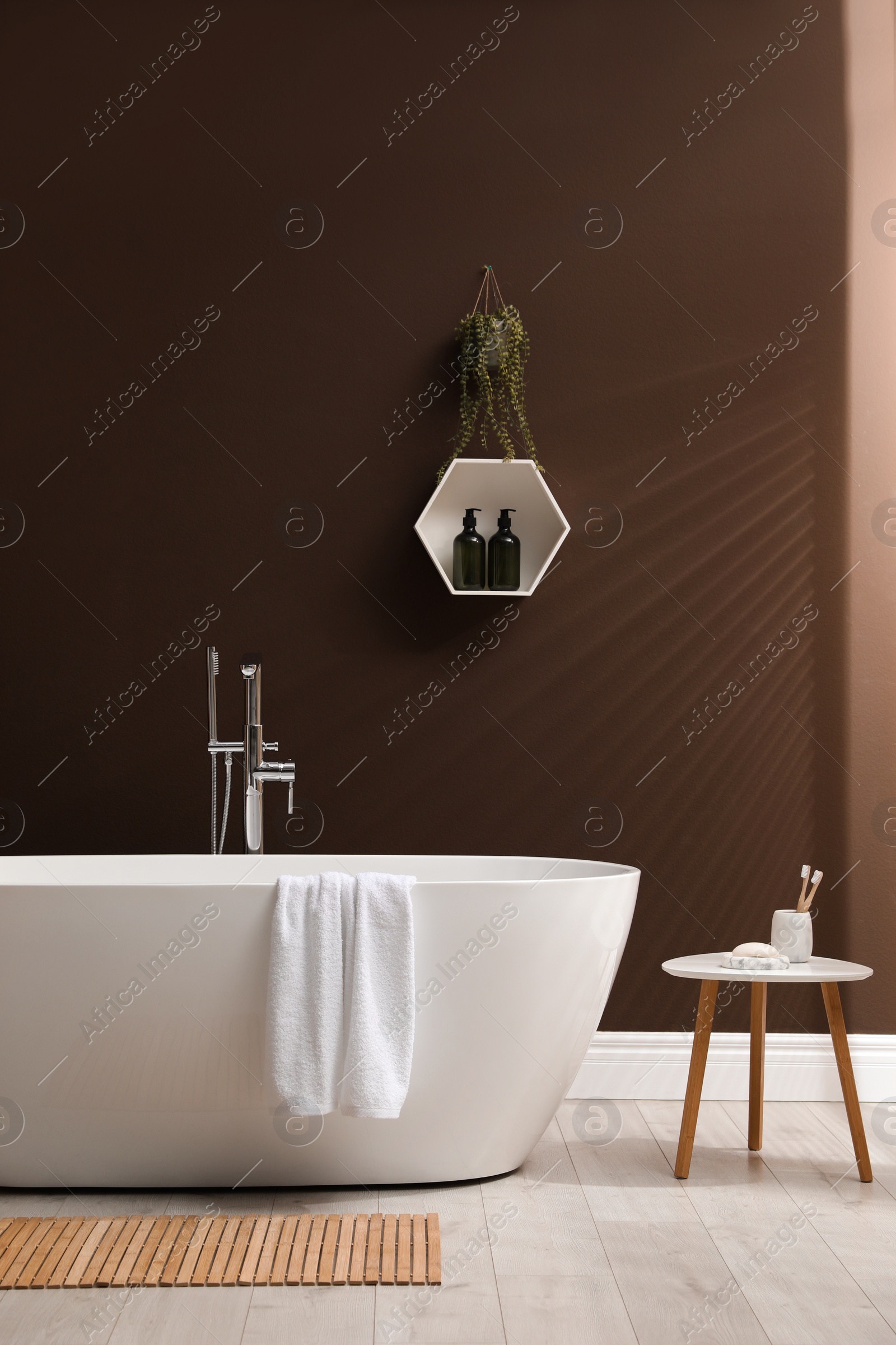 Photo of Modern ceramic bathtub with towel near brown wall in room