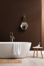 Modern ceramic bathtub with towel near brown wall in room