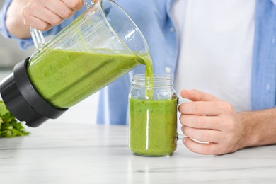 Photo of Man pouring delicious smoothie into glass at white marble table indoors, closeup