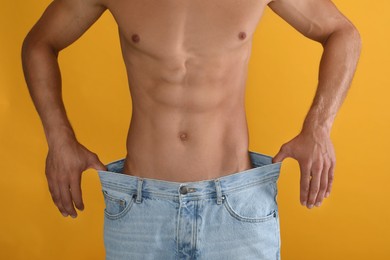 Photo of Shirtless man with slim body wearing big jeans on yellow background, closeup