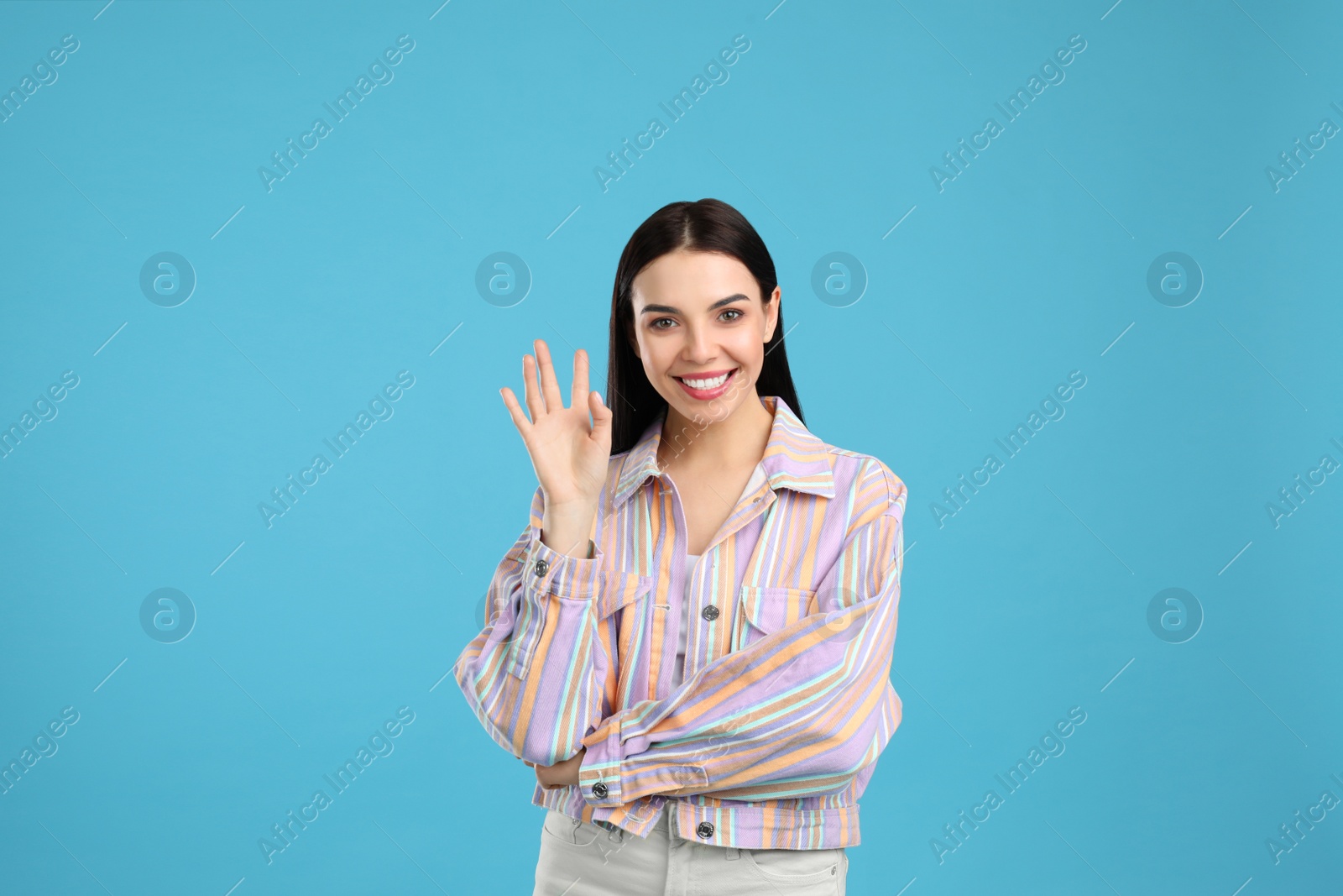 Photo of Attractive young woman showing hello gesture on light blue background