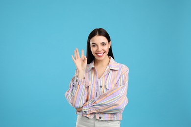 Attractive young woman showing hello gesture on light blue background