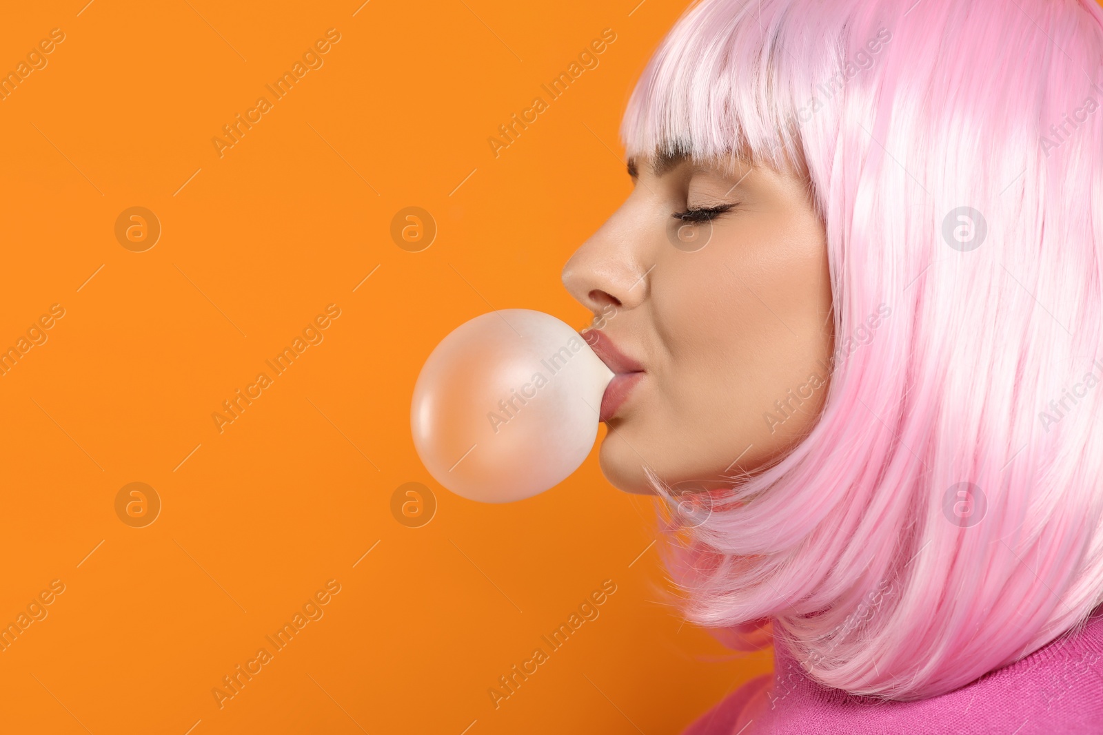 Photo of Beautiful woman blowing bubble gum on orange background, space for text