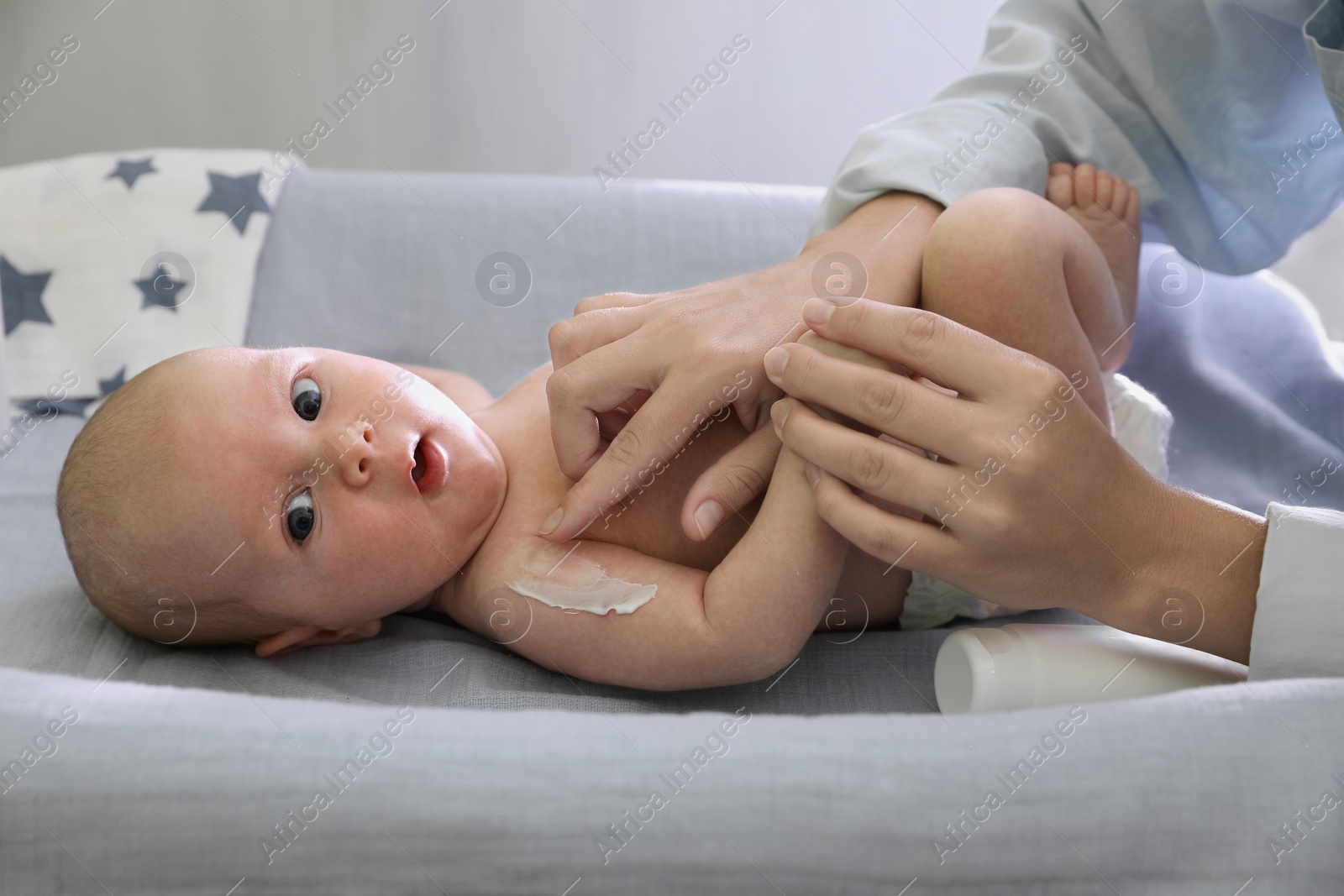 Photo of Mother applying moisturizing cream onto baby`s arm on changing table indoors, closeup