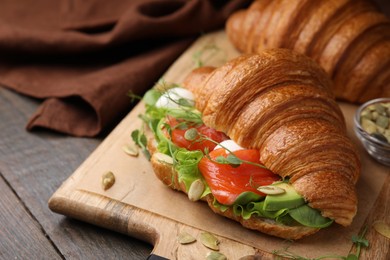 Photo of Tasty croissant with salmon, avocado, mozzarella and lettuce on wooden table, closeup