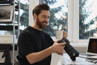 Professional photographer with digital camera and cup of drink at table in office