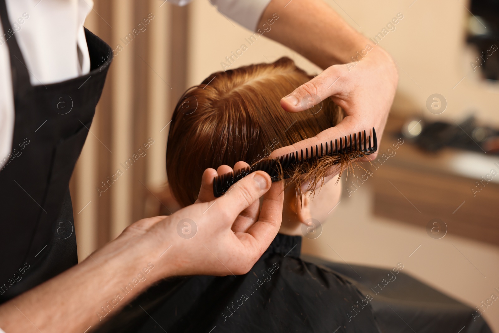 Photo of Professional hairdresser combing boy's hair in beauty salon, closeup