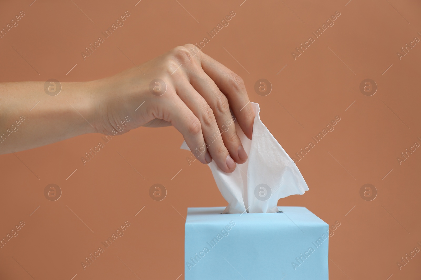 Photo of Woman taking paper tissue from box on light brown background, closeup