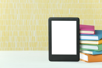 Photo of Portable e-book reader and stack of books on white wooden table, space for text