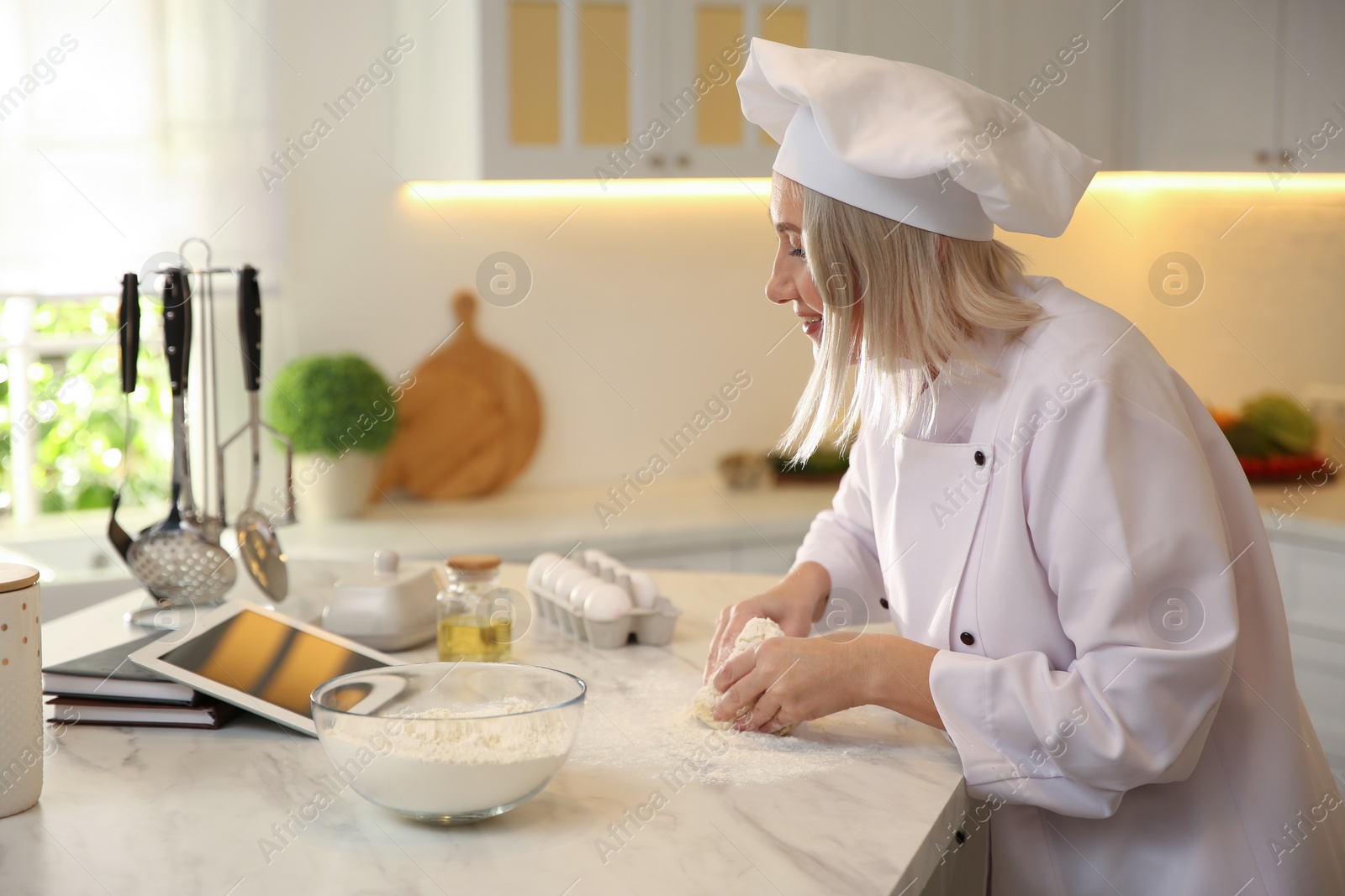Photo of Chef with tablet cooking dough at table in kitchen