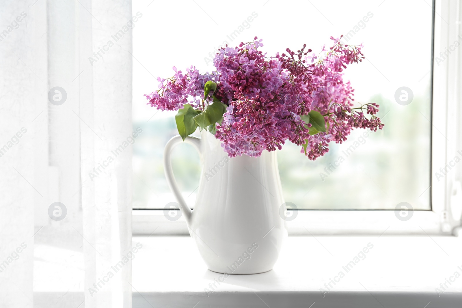 Photo of Jug with beautiful blossoming lilac on window sill. Spring flowers